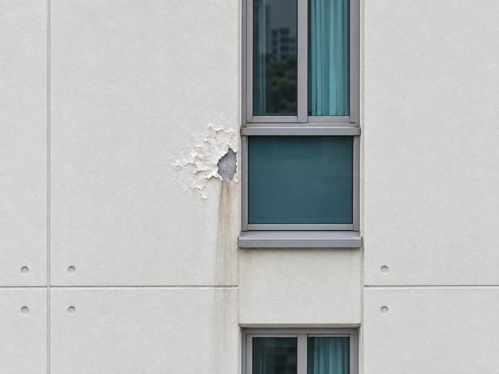 Close-up of a rendered wall beside a window with damaged paint and staining