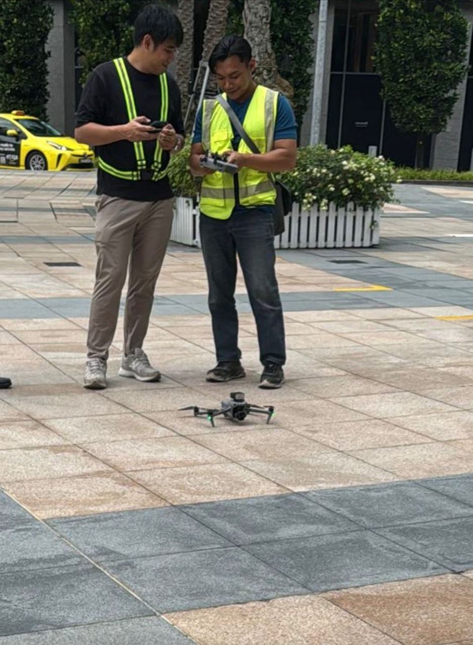 An operator and a facade inspector in high-visibility vests on site, with the operator's controller and a drone on the ground